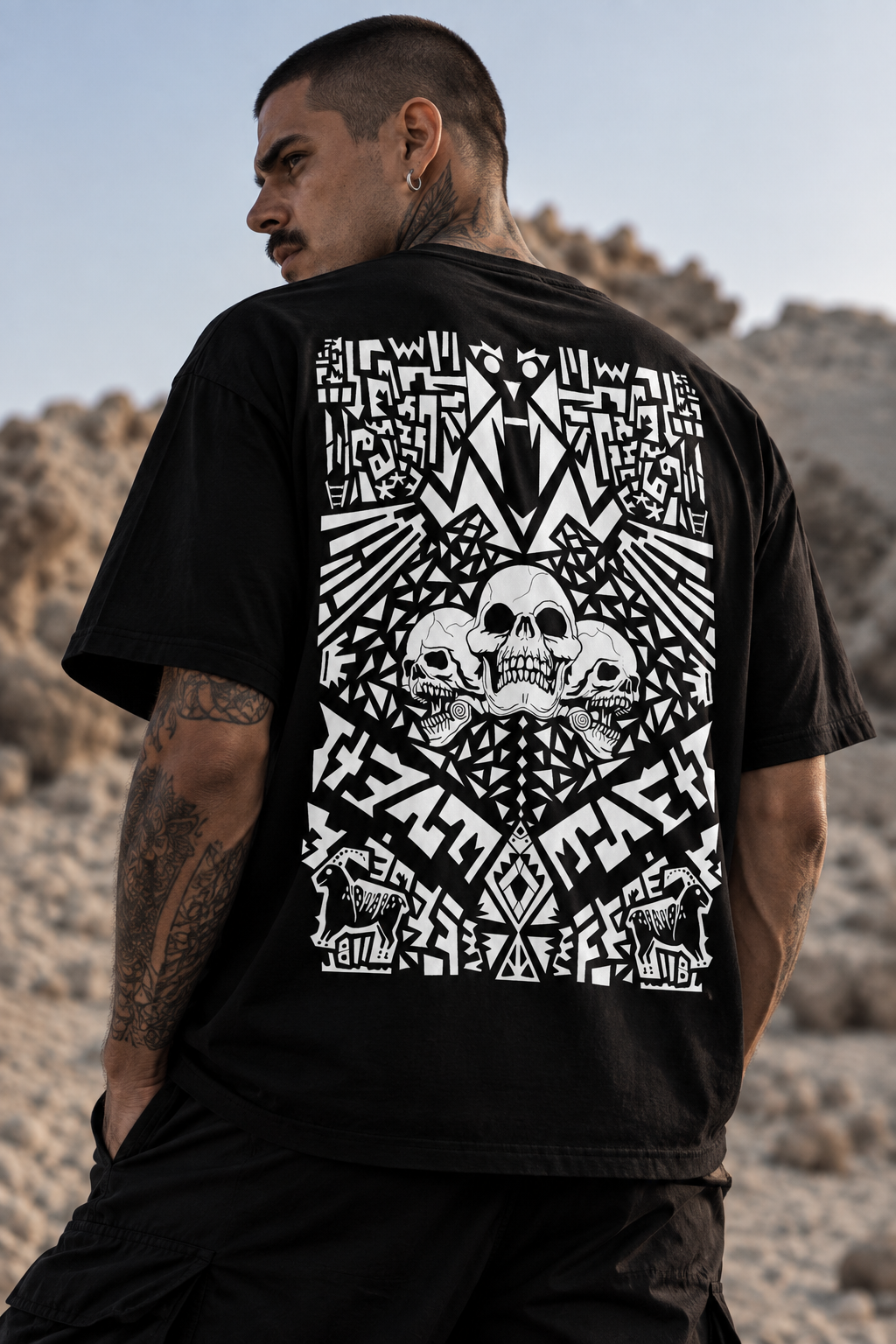 A man wearing a black LMNO t-shirt with a large white graphic print on the back, standing in a rocky desert landscape.