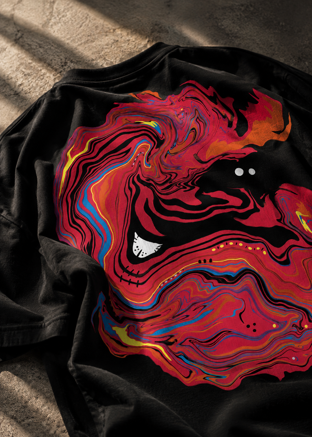 A black LMNO T-shirt laid flat on a textured concrete surface, featuring a large abstract marbled graphic in red, orange and yellow.