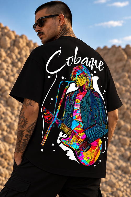 A man wearing a black LMNO graphic t-shirt with a colorful, psychedelic illustration of text "Cobaine" on the back, set against a desert rock landscape.