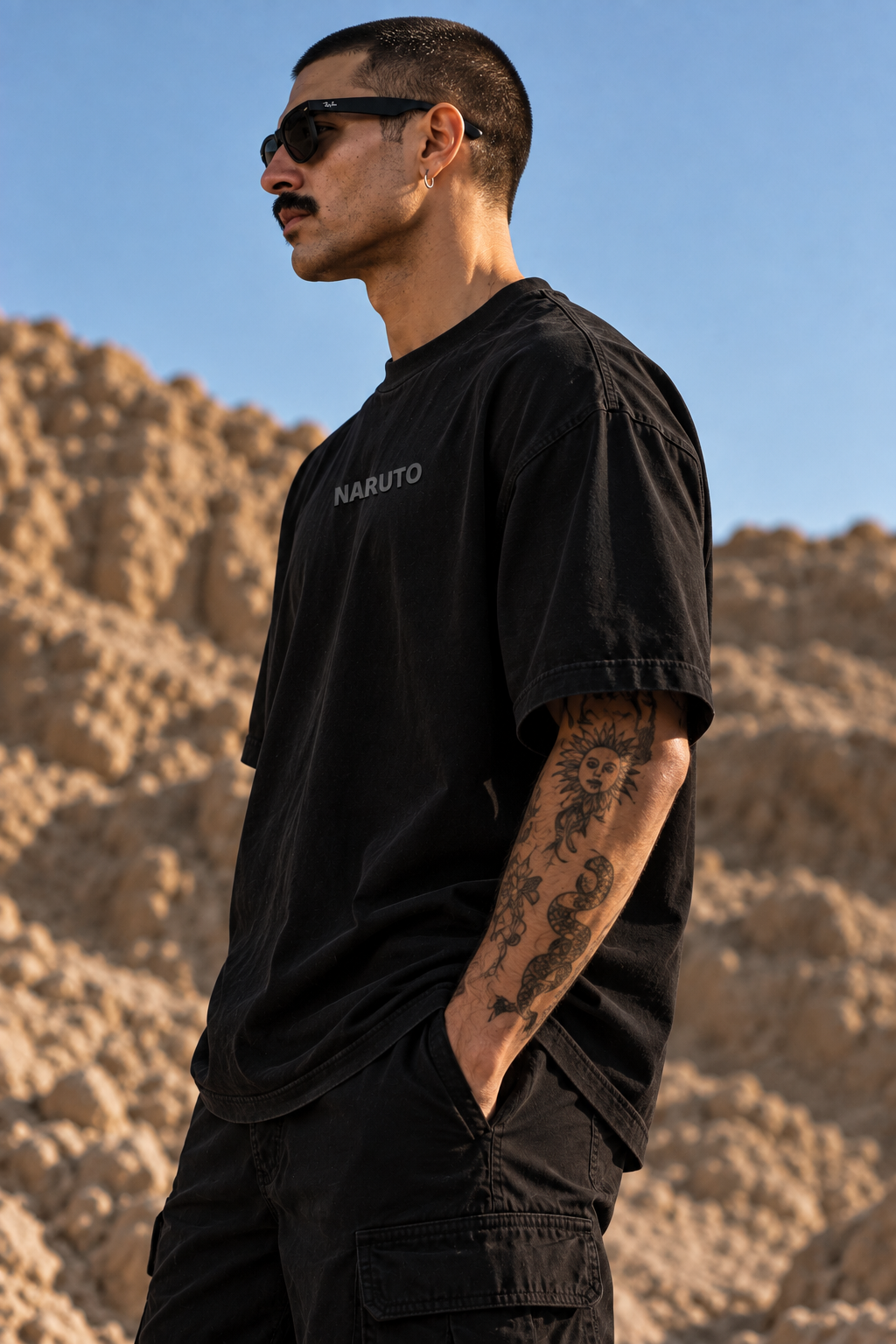 A man wearing a black LMNO t-shirt with 'NABUTO' printed on the chest, standing outdoors against a rocky desert background under a blue sky.