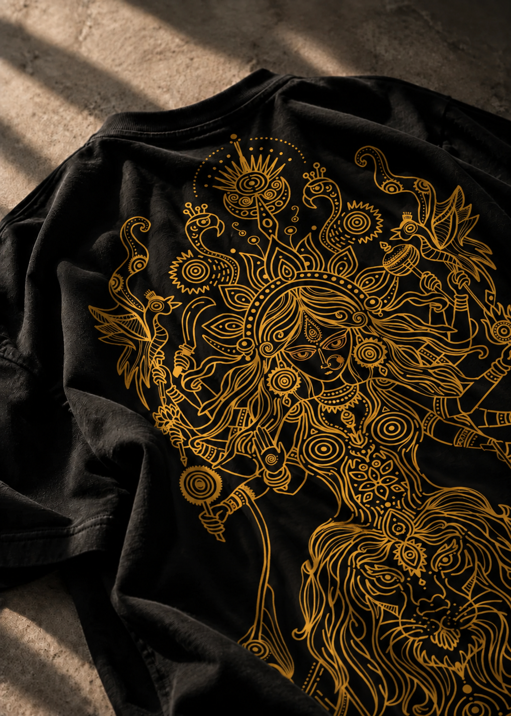 A Black Oversized LMNO Tshirt lying on a concrete floor with its back displaying an intricate golden Goddess Durga.