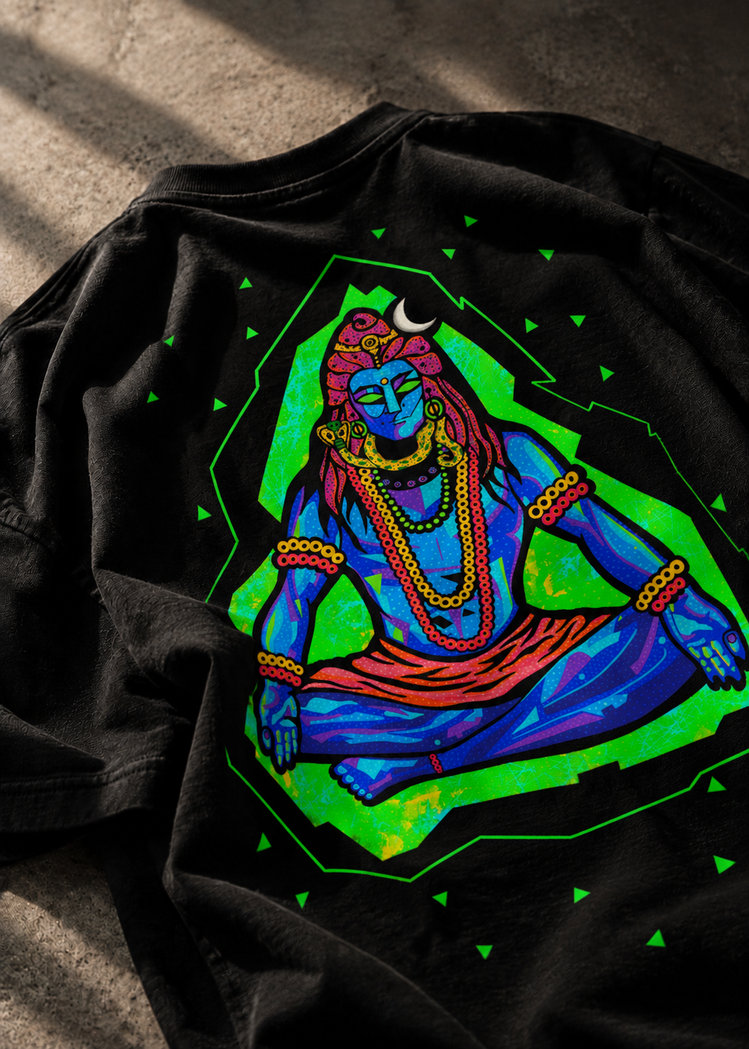 A black LMNO t-shirt laid flat on a textured concrete surface, featuring a vibrant, colorful graphic of a meditating Lord Shiva.