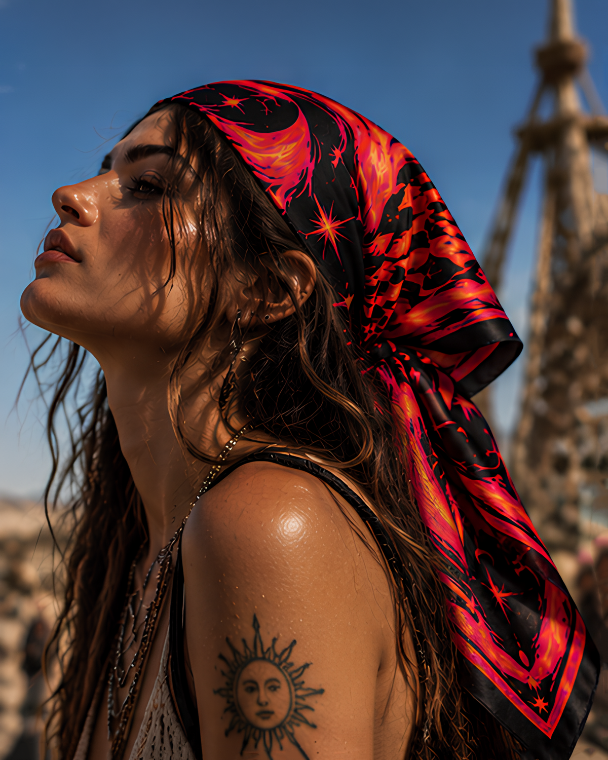 A woman outdoors wearing a red and black patterned silk LMNO headscarf with a crescent moon and star design. The Eiffel Tower is visible in the blurred background under a blue sky.