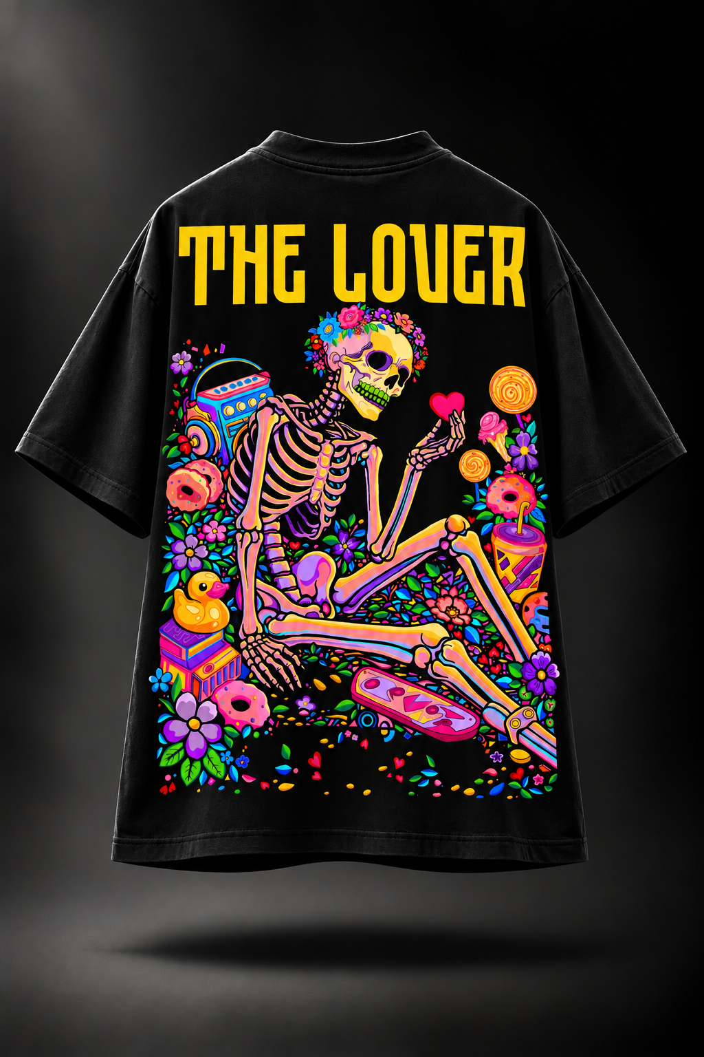 A black oversized LMNO t-shirt with a vibrant, colorful graphic on the back. The graphic features the yellow text 'THE LOVER' above a Day of the Dead skeleton sitting with donuts, flowers, and a heart, set against a dark studio background.