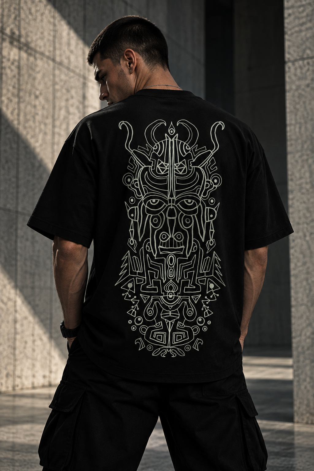 A man viewed from behind wearing a black LMNO t-shirt with a large white Aztec skull graphic on the back, standing in front of a gray stone wall.