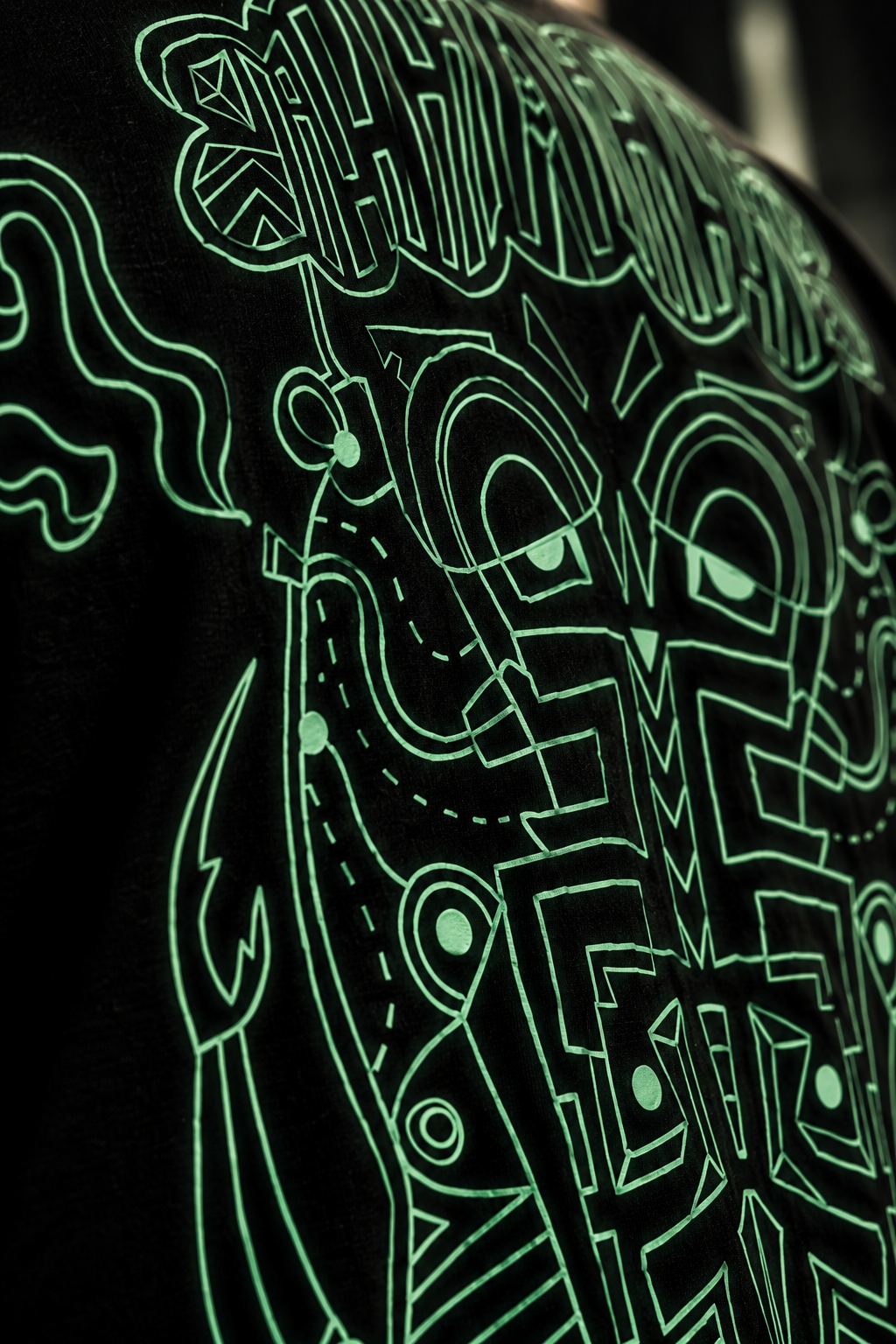 Close-up of a black LMNO tshirt featuring a glowing neon green graphic print with stylized lettering and abstract line art.